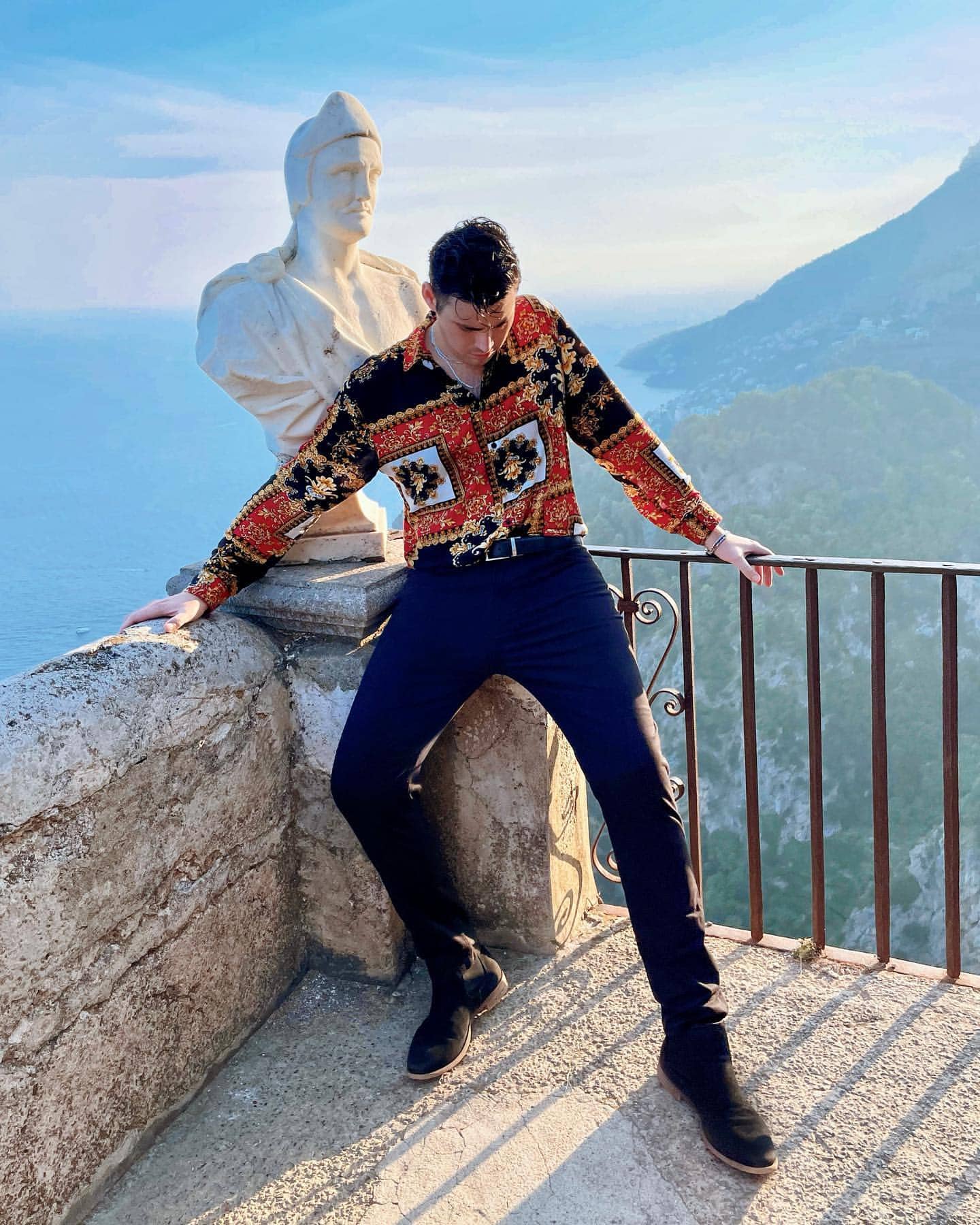 Actor Troy Bronson wearing a baroque-style long sleeve shirt at a balcony in Ravello on the Amalfi Coast, Italy, showcasing historic statues.