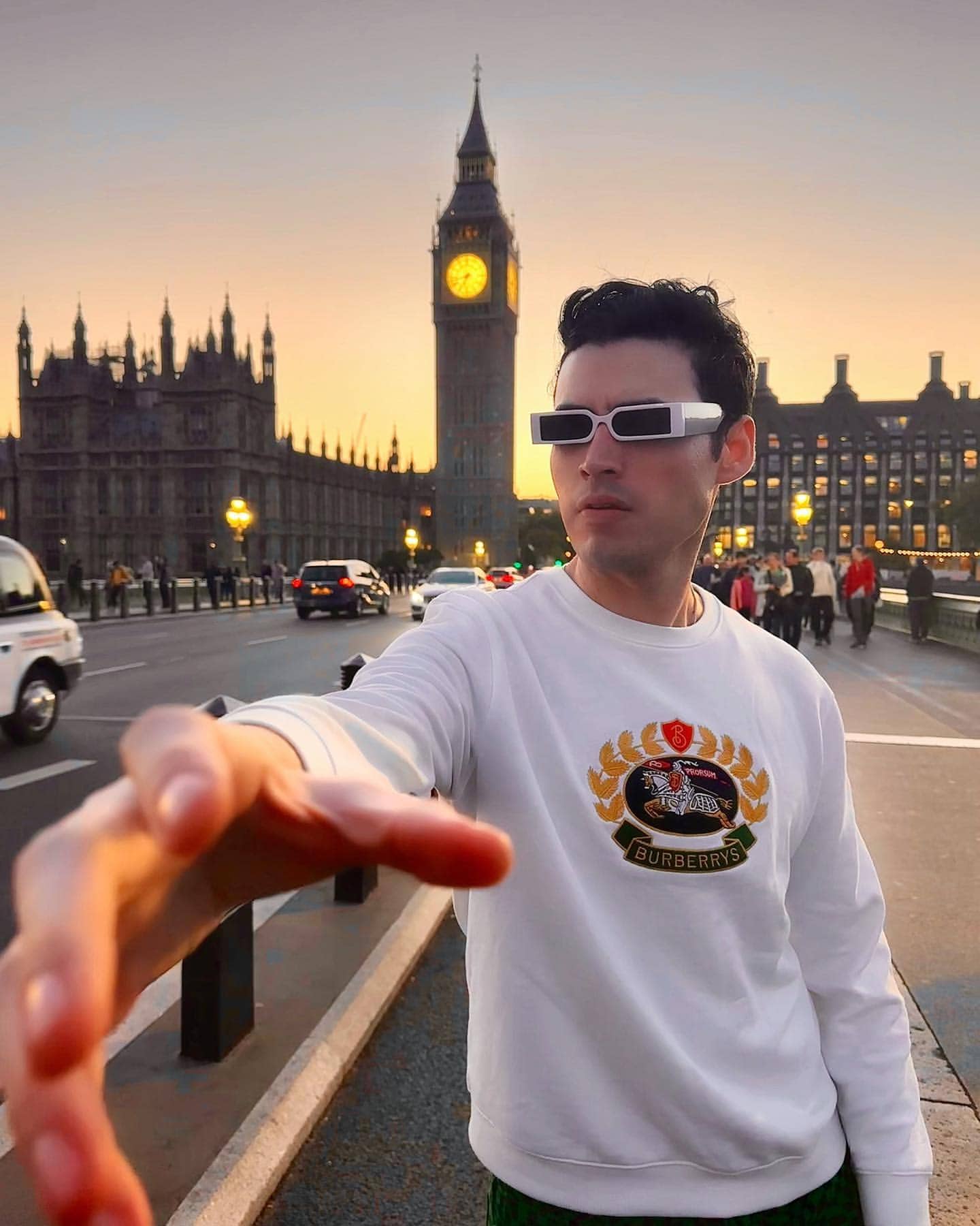 Troy Bronson, Actor, striking a cool pose in a white Burberry outfit and sunglasses, with the stunning sunset-lit Big Ben in the background.